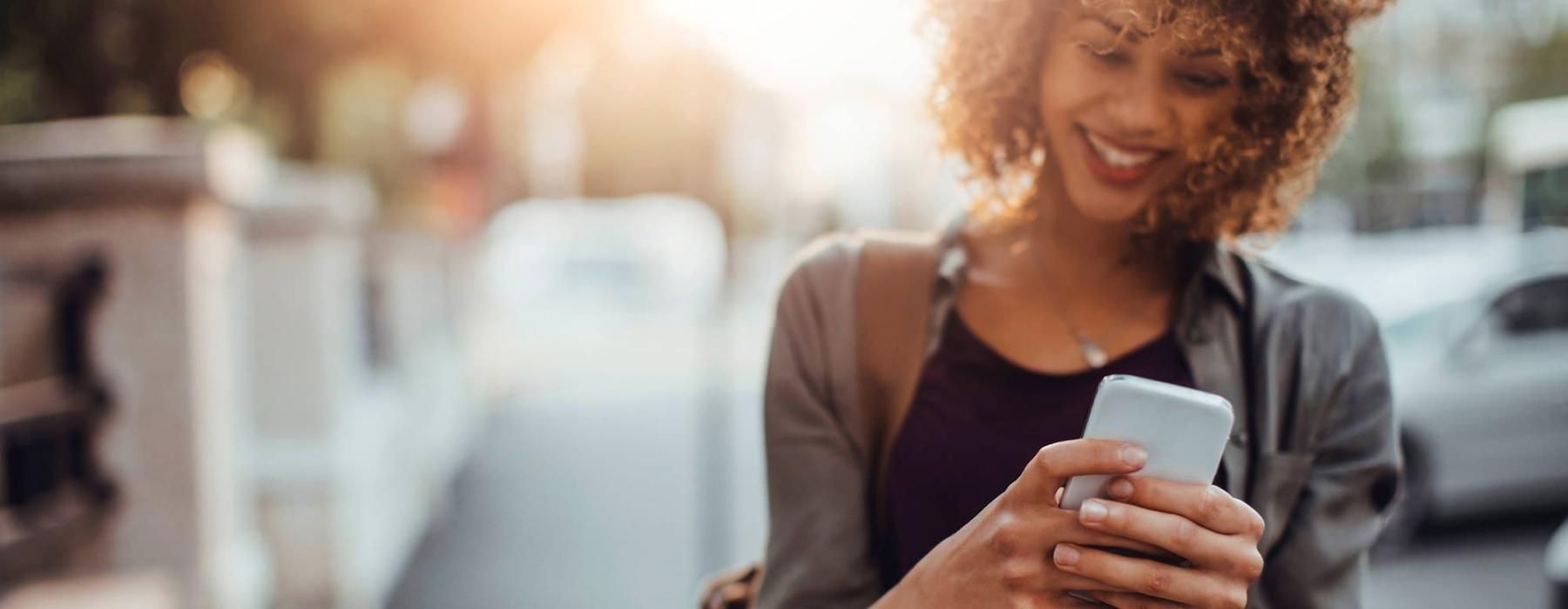 woman texts on her phone as she walks through the city